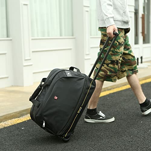 Person pulling a black rolling bag on a street.